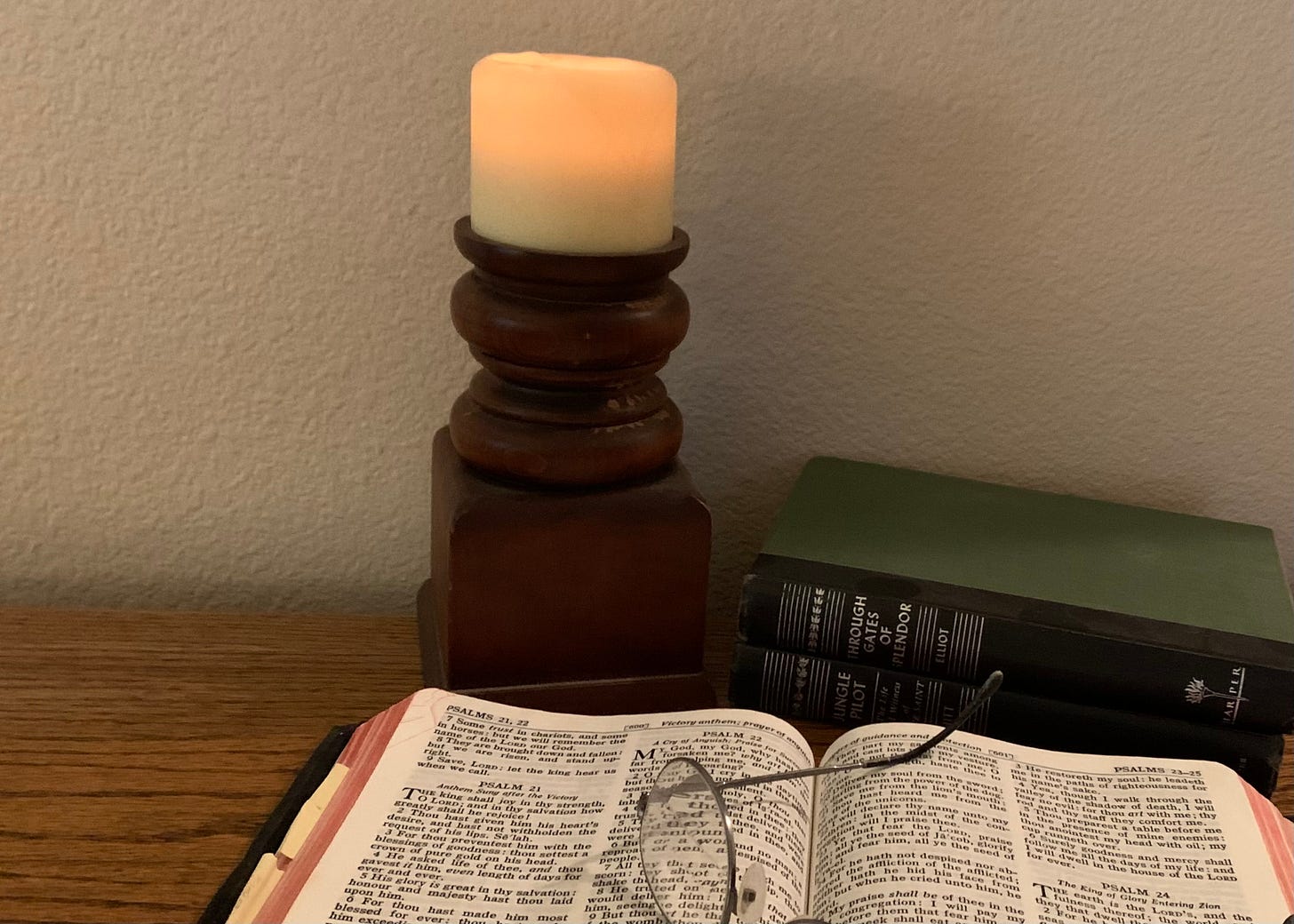 Image of an open Holy Bible with glasses set upon, and two books and a candle beside.