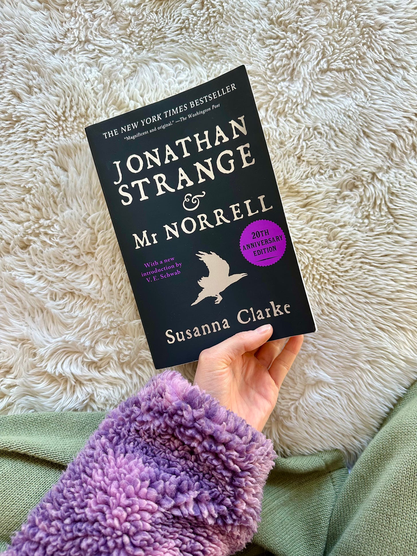 A white hand holds a copy of Jonathan Strange & Mr Norrell against a white blanket