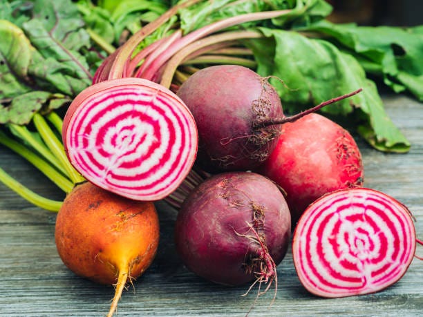 A group of multicolored beets including a Chiogga beet sliced open to the the pine and white interior