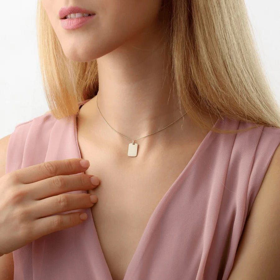 Blonde woman in a pink v neck wearing the gold tag necklace by Sarah Elise.