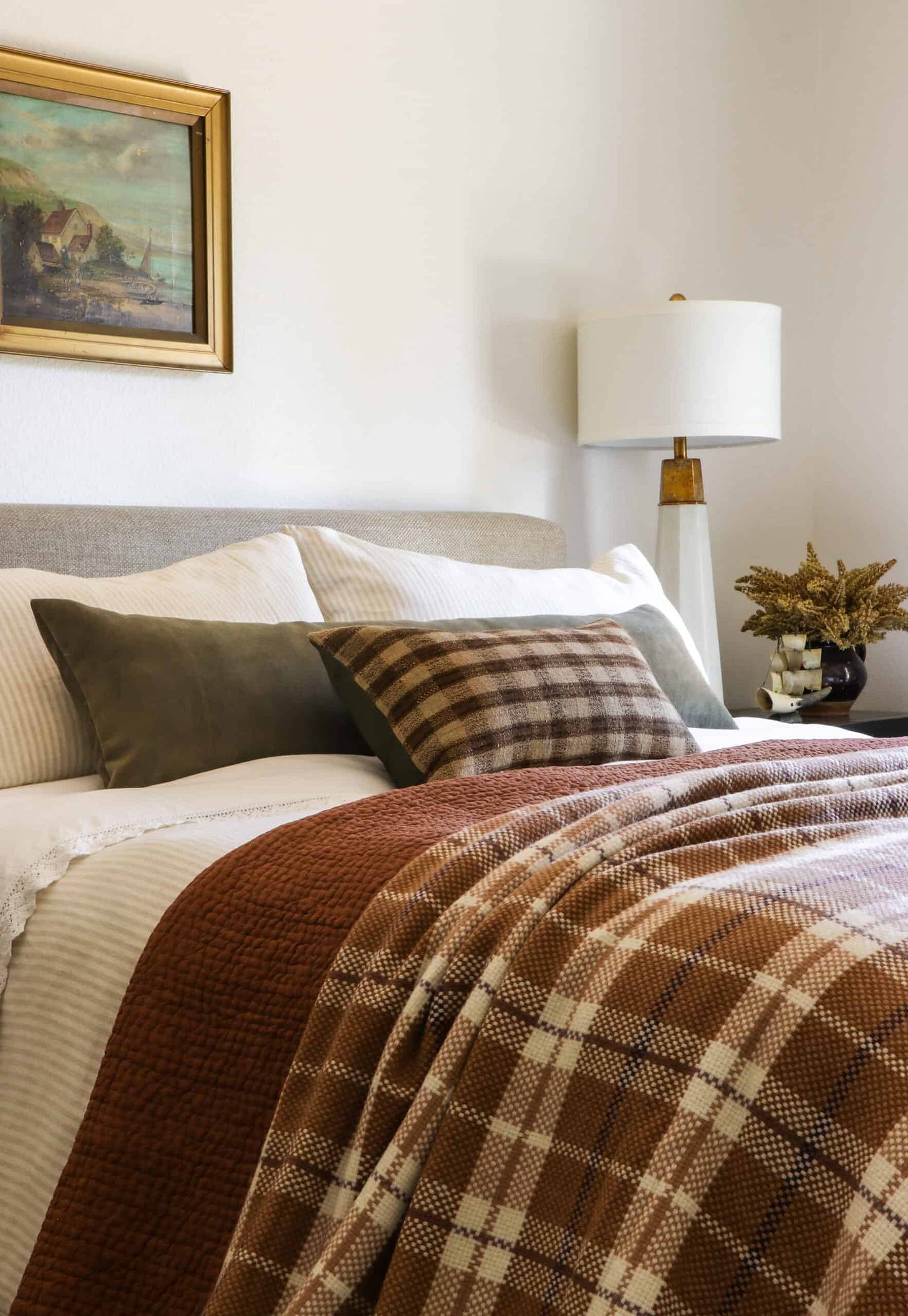 plaid and rust bedding on bed with oil painting above