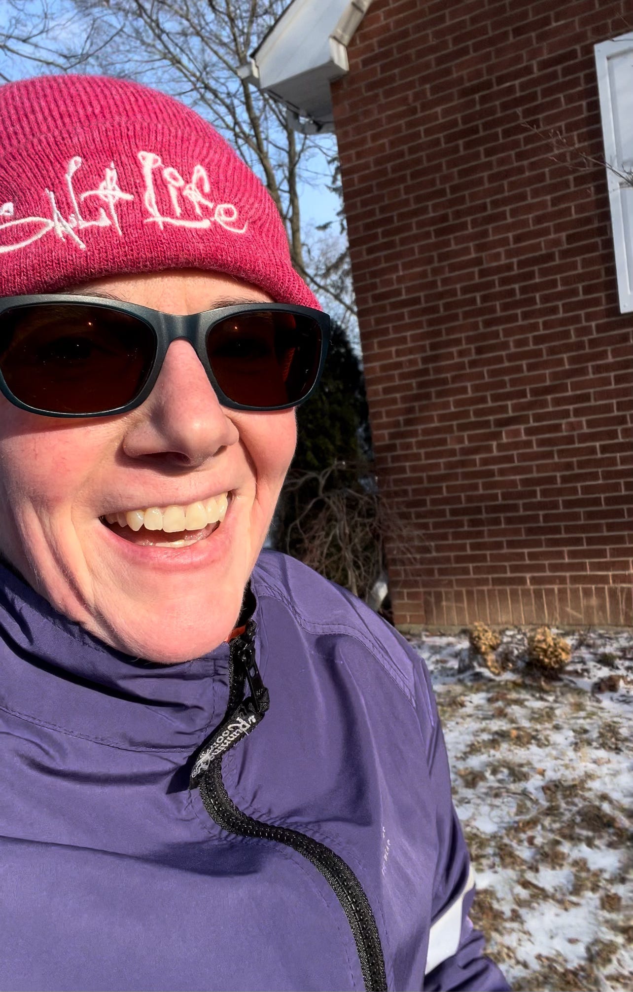 Woman smiling, running in the cold wearing a pink toque, purple jacket and sunglasses