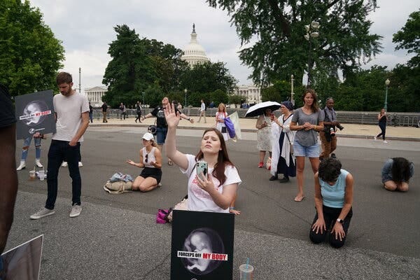 Anti-abortion demonstrators standing, kneeling and praying on the street, with the Capitol in the background.