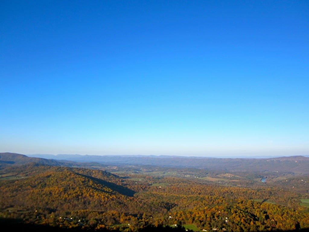 A view looking out across low mountains with orange foliage, the sky bright blue