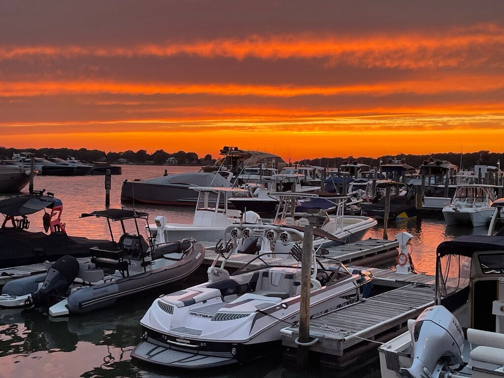 A photograph of a sunset over a dock full of boats.