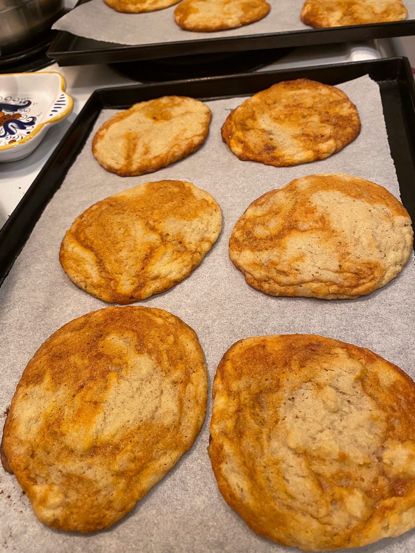 On a black baking pan lined with parchment, six large sugar cookies with orange-y stripes of gochujang caramel. Another pan of the same is just visible in the backgrond at the edge of the frame.