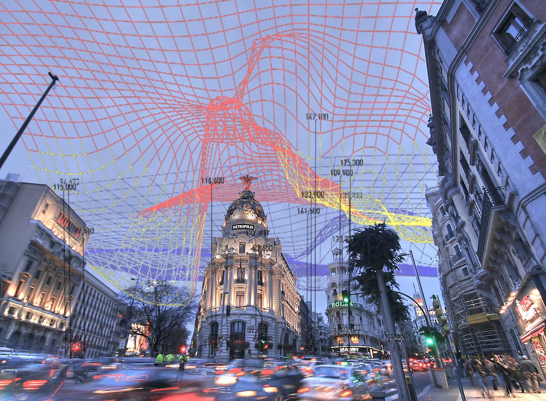 Photo of the Metropolis building in central Madrid taken with long exposure, so that traffic appears blurred. A grid of different colour computer-generated lines are overlaid in the sky.