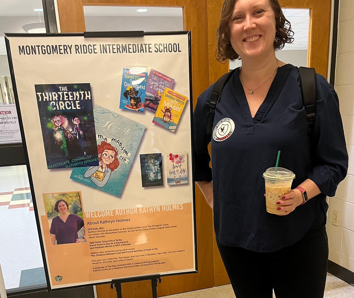 Kathryn at a recent school visit, posing with a poster showing all of her published books including The Thirteenth Circle.