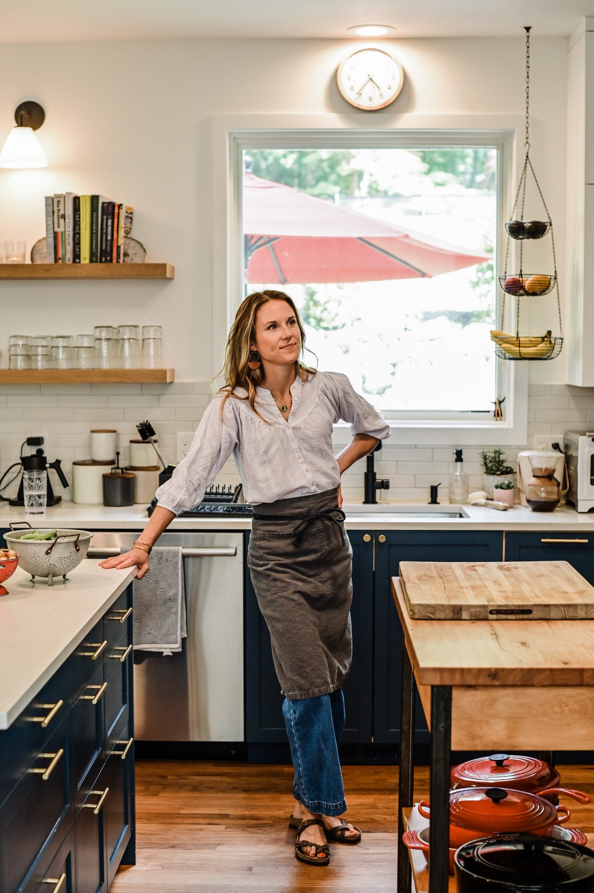 Nicki wearing a white top, blue jeans and a grey apron standing in her kitchen.