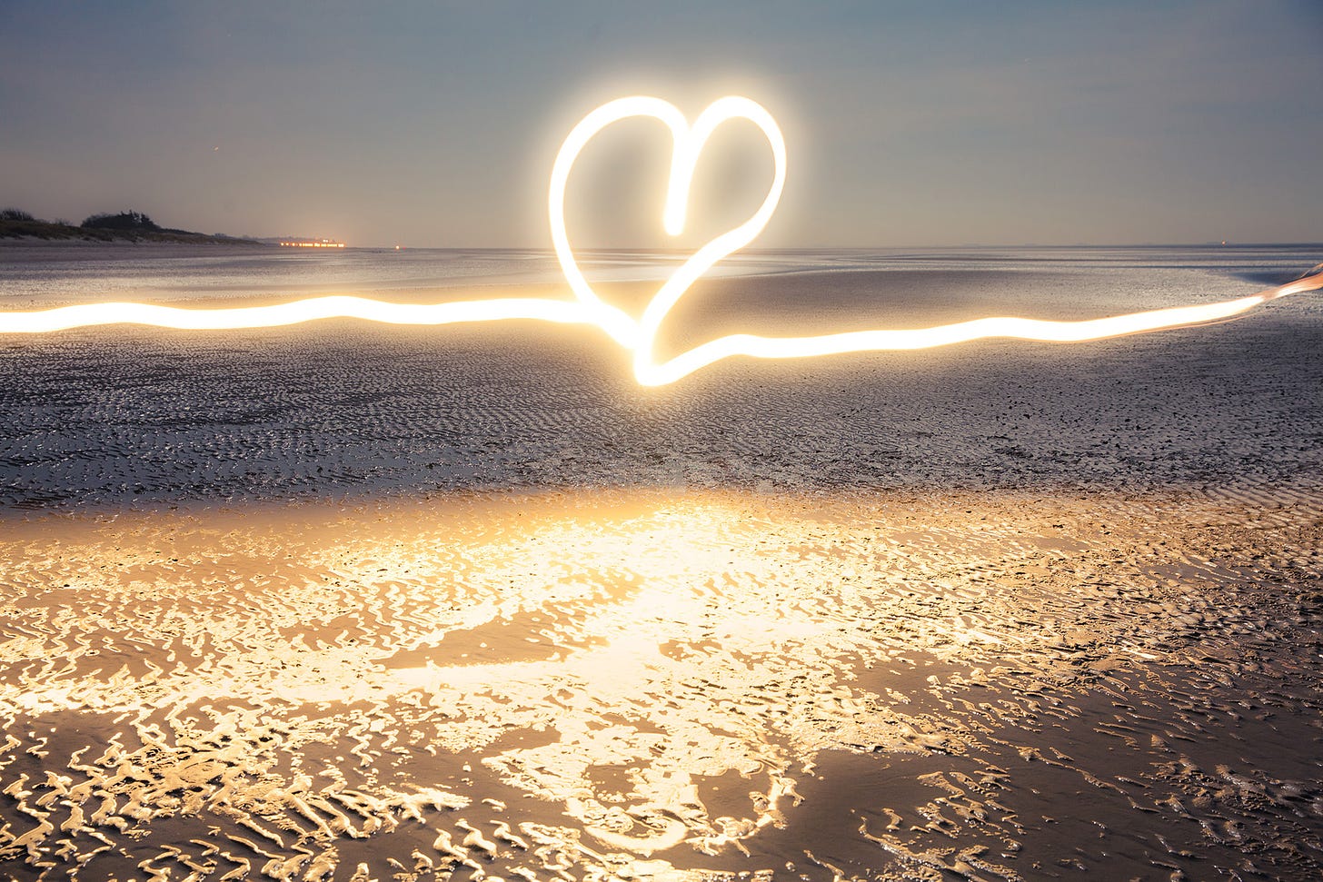 A glowing heart drawn with flashlight at blue hour on the beach near the water at low tide