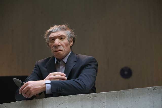A Neandertal artist's reconstruction at the Neanderthal Museum, wearing a suit and holding a stone tool.