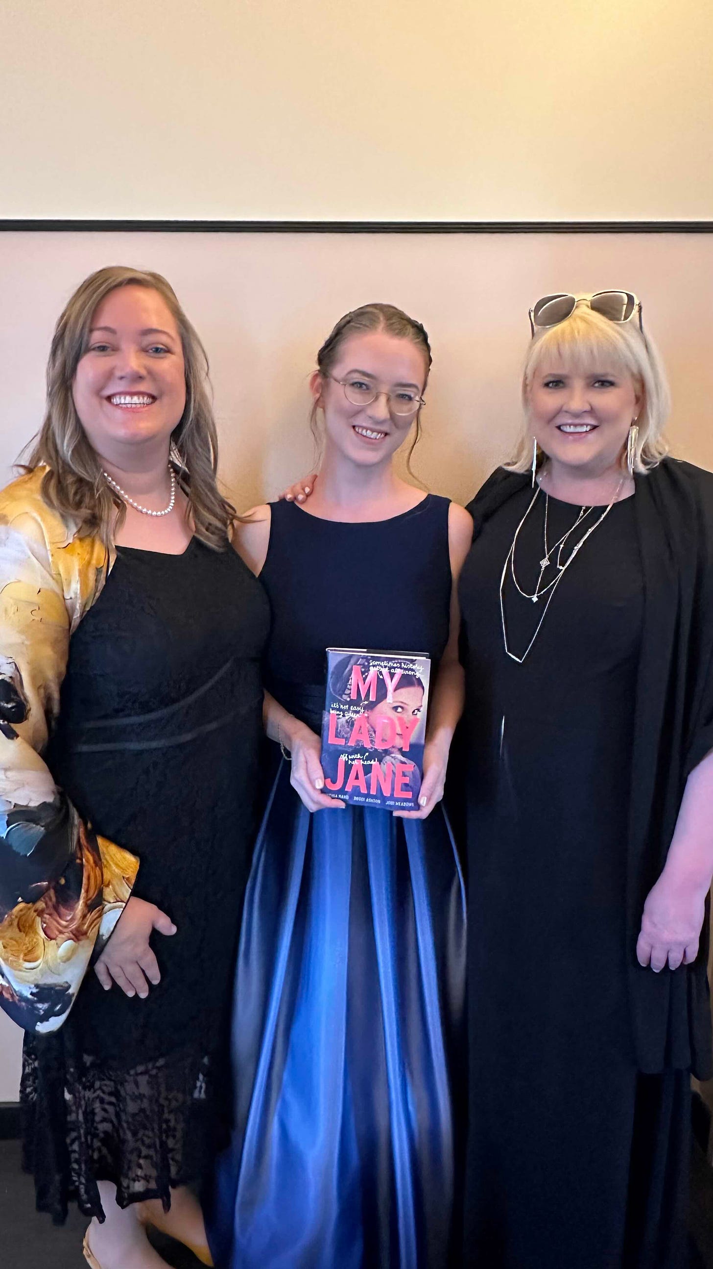 Janies all dressed up: Cynthia is wearing a black dress and a yellow and black silk shawl; Jodi is wearing a blue dress and holding the book; Brodi is wearing a black dress and many necklaces.