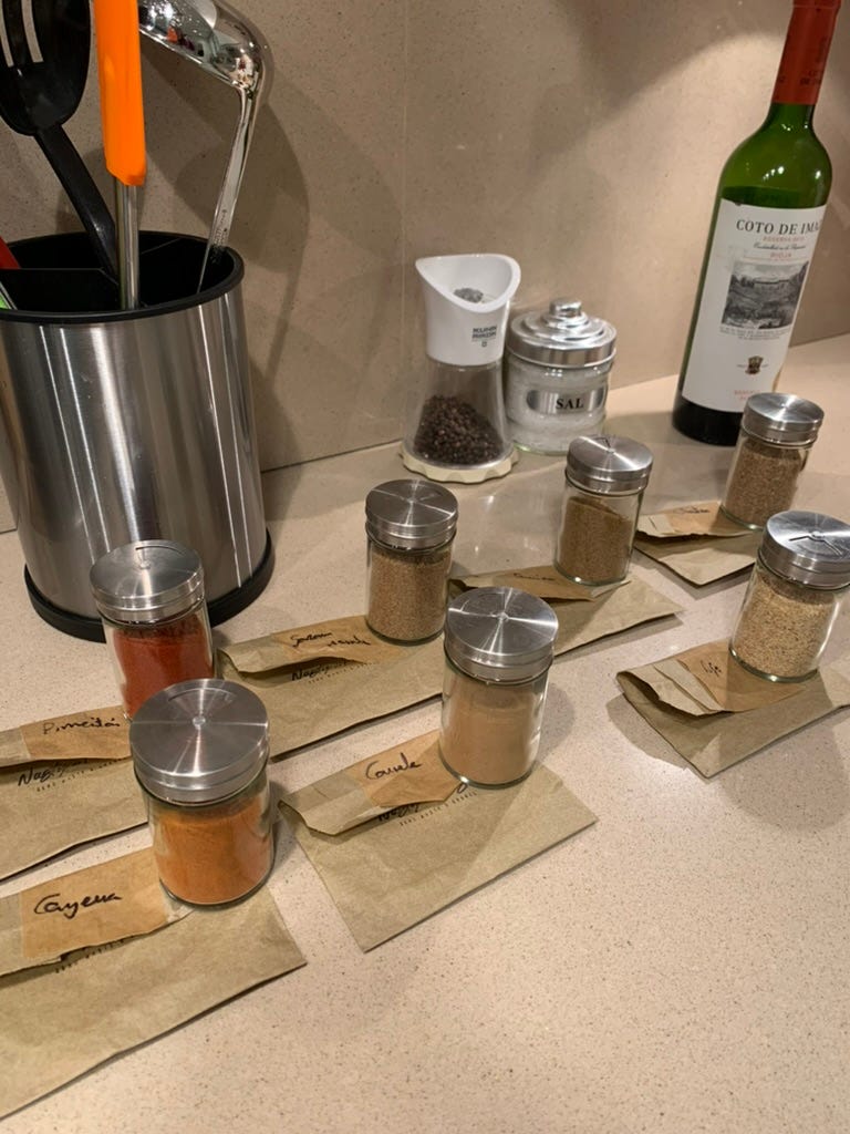 Newly filled spice jars on the kitchen counter sitting on the labled paper bags from the store they came from.