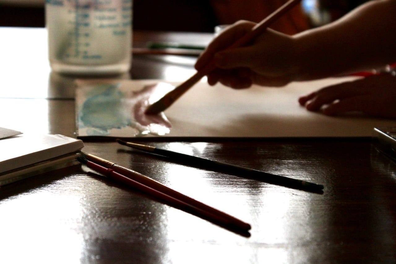 Paintbrushes, a small hand painting, sunlight reflecting off the table