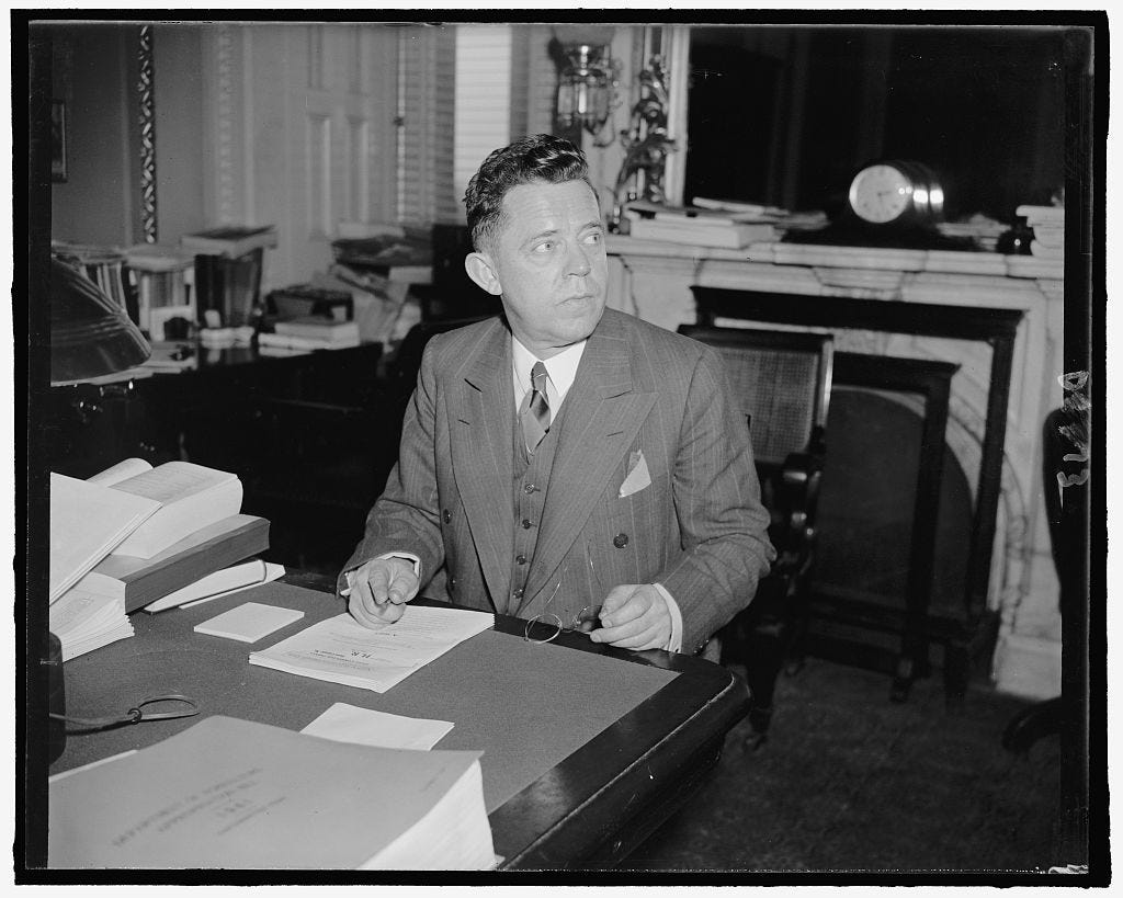 Rep. Ralph Church (R-IL), 1940 seated at his desk in front of a fireplace. He's wearing a suit and tie.