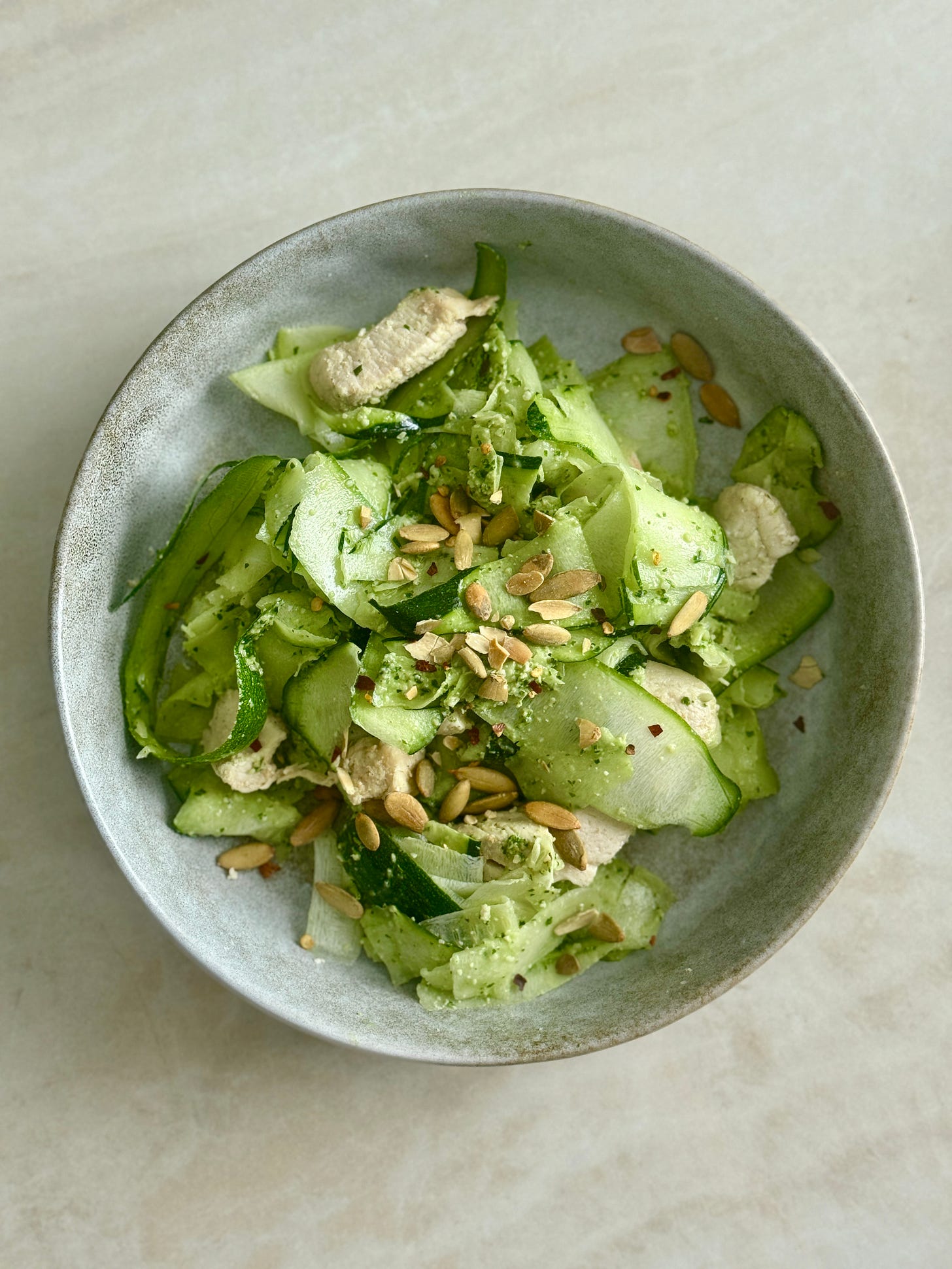 Zucchini noodles tossed with brown rice, chicken tenderloins, pumpkin seeds, and herby green macadamia sauce for a vibrant, low-carb, high-protein bowl.