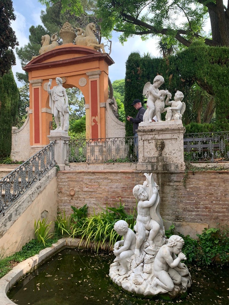 a small pond with a statue of children holding a dolphin; up some stairs Bacchus raises a glass, some cherubs feed a dog something he probably shouldn't be eating, and two mer-horses sit atop an arched gateway