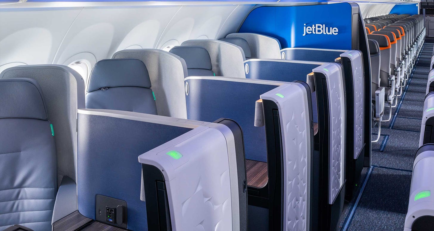 Business class seat on single aisle aircraft from JetBlue, with seats tucked near the window and surrounded by walls with a narrow access route from the airplane aisle.
