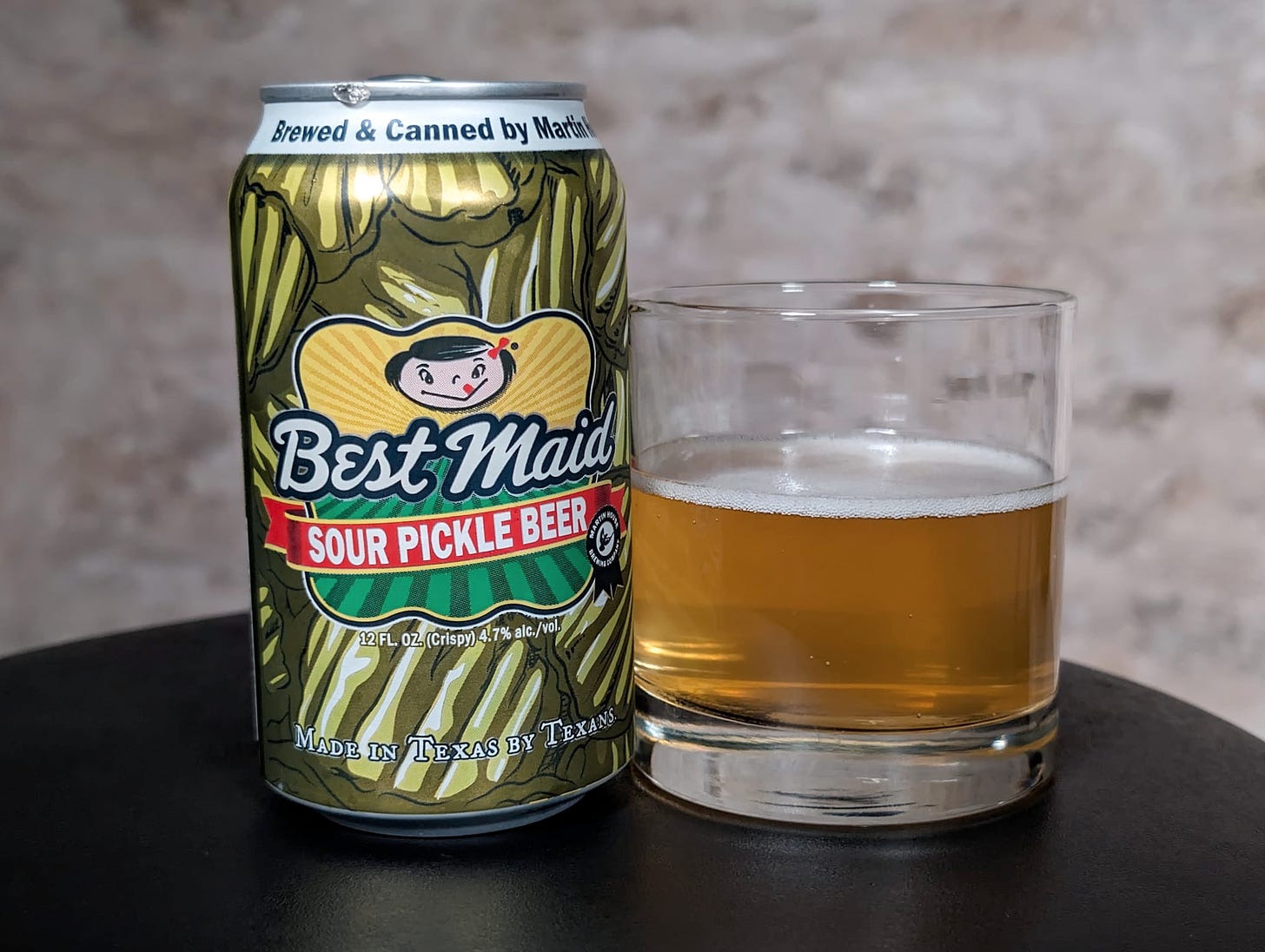 A can of "Best Maid Sour Pickle Beer" right next to a round glass halfway filled with it