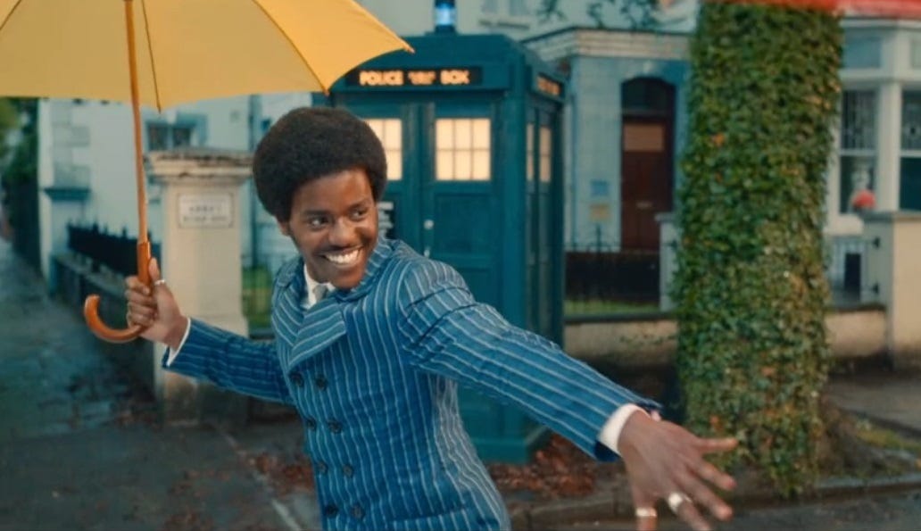 The Doctor (Ncuti Gatwa) as the Doctor dancing on Abbey Road in a natty suit with an umbrella in his right hand and the TARDIS behind him, from the episode The Devil's Chord