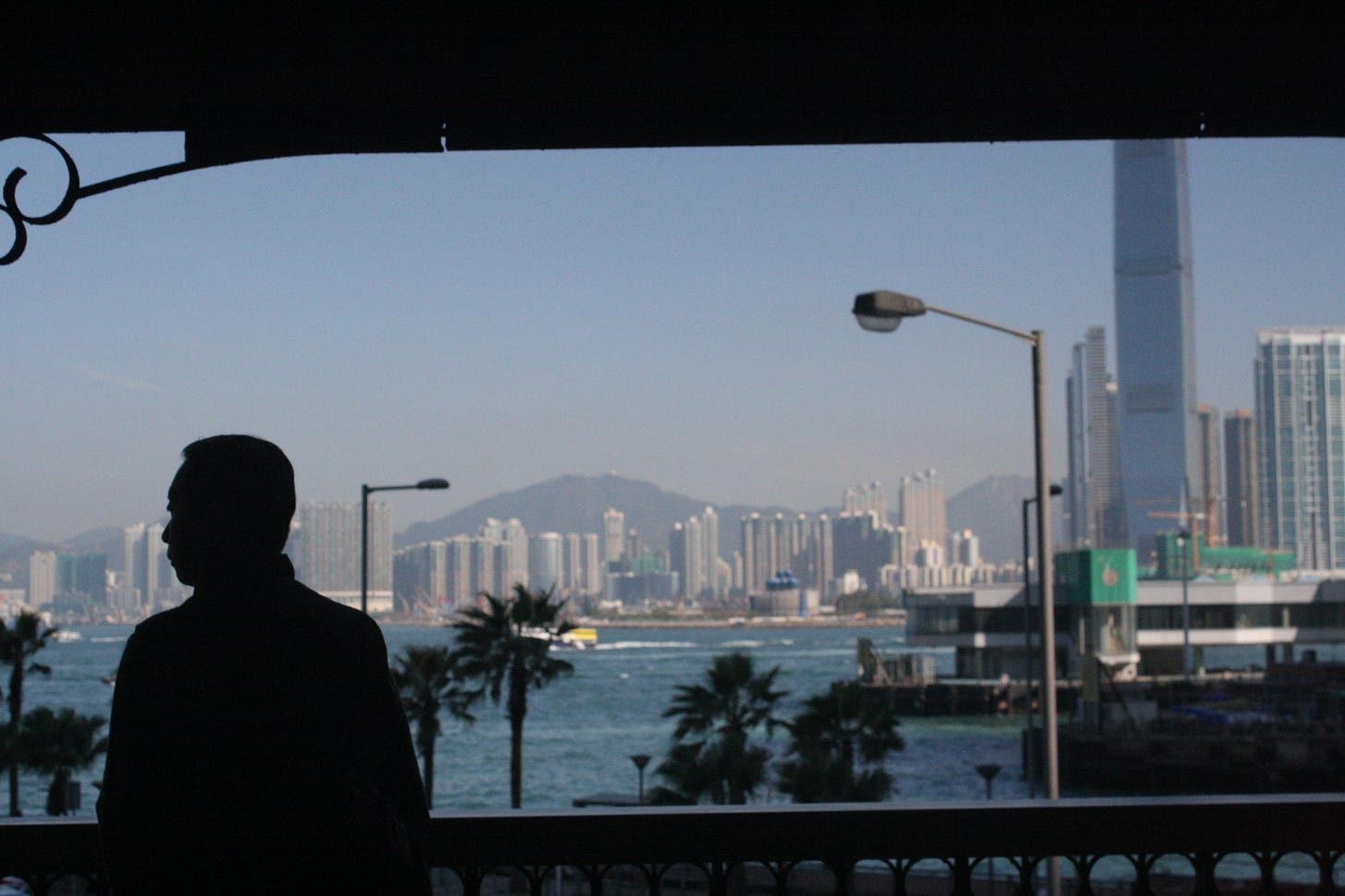 Foto da skyline de Hong Kong, em que a silhueta de um homem está em primeiro plano e ele olha para o lado.
