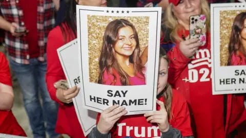 Getty Images Women wearing red Trump 2024 T-shirts hold up signs with Laken Riley's photo and the words "say her name!"