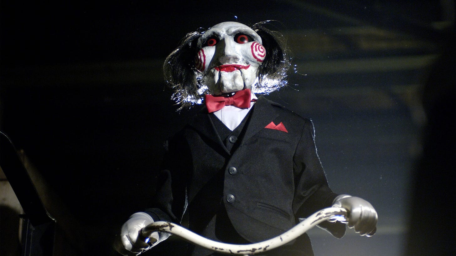 Movie still from Saw. A creepy clown puppet of Jigsaw wearing a bowtie