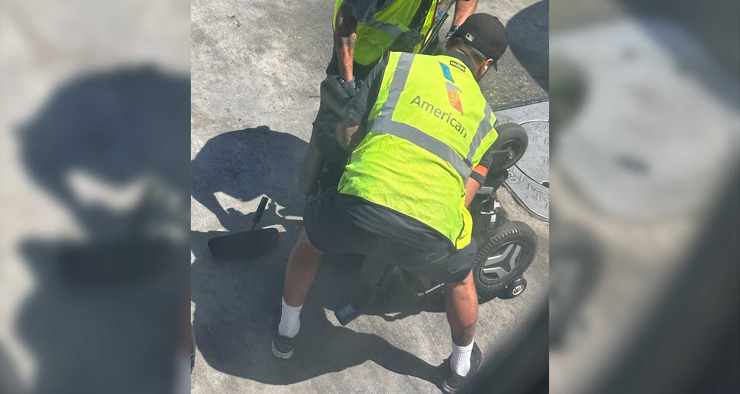 Power wheelchair flipped upside down on the pavement, with two American Airlines ground staff members around it.