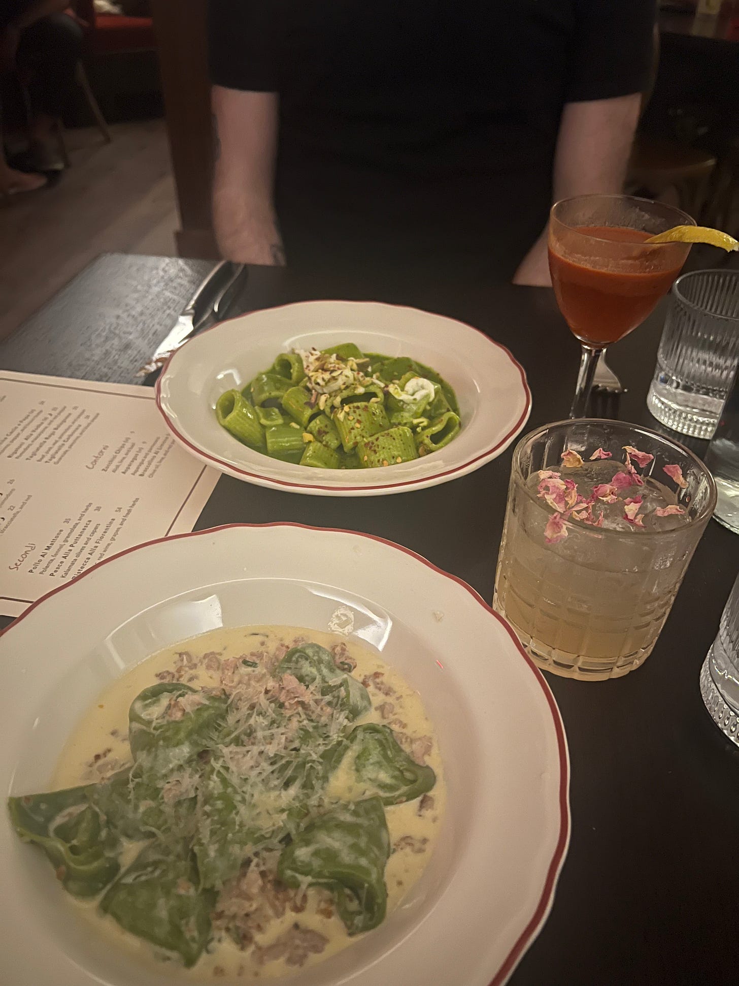 Two bowls of green pasta and two cocktails on a table