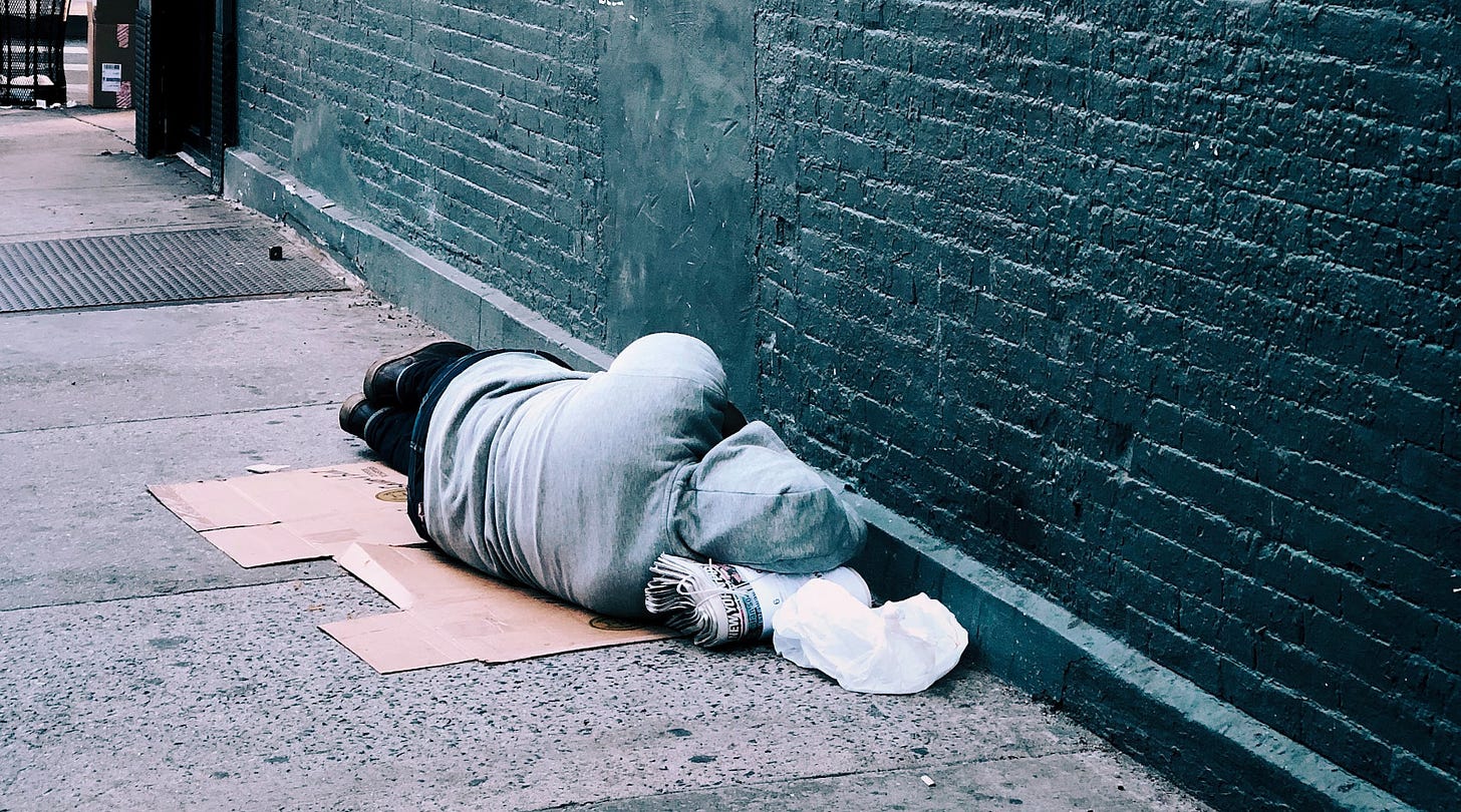 Person sleeping on sidewalk next to building.