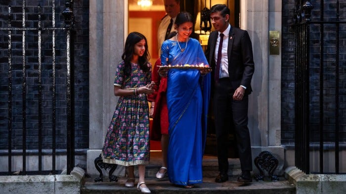 Rishi Sunak stands next to his wife, who is carrying a tray of lighted candles, outside Downing Street. Their two daughters are with them