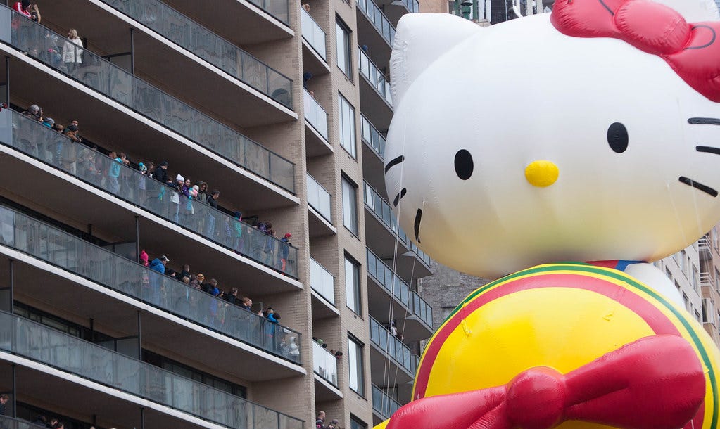 An enormous hello kitty flies her balloon plane by some apartment buildings