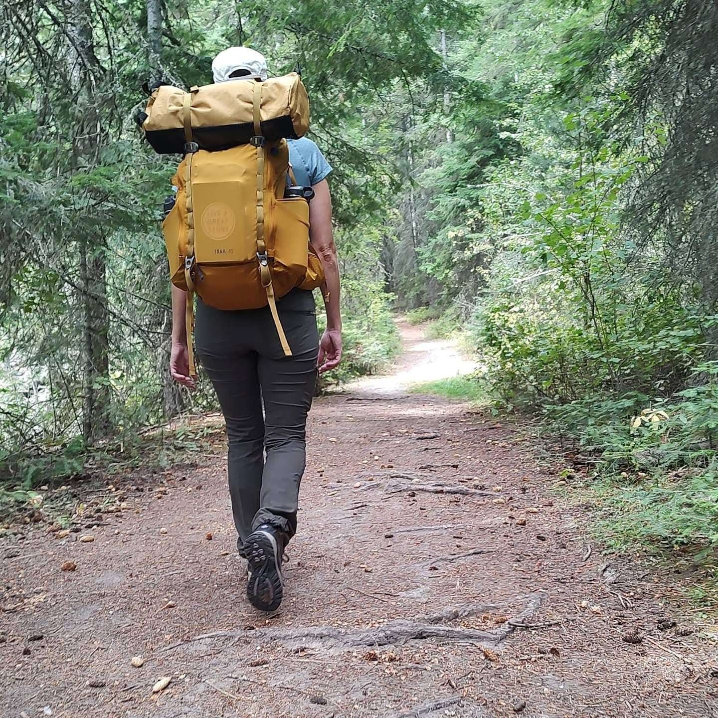 photo of the author with a large yellow backpack, hiking away from the camera, on a wooded trail