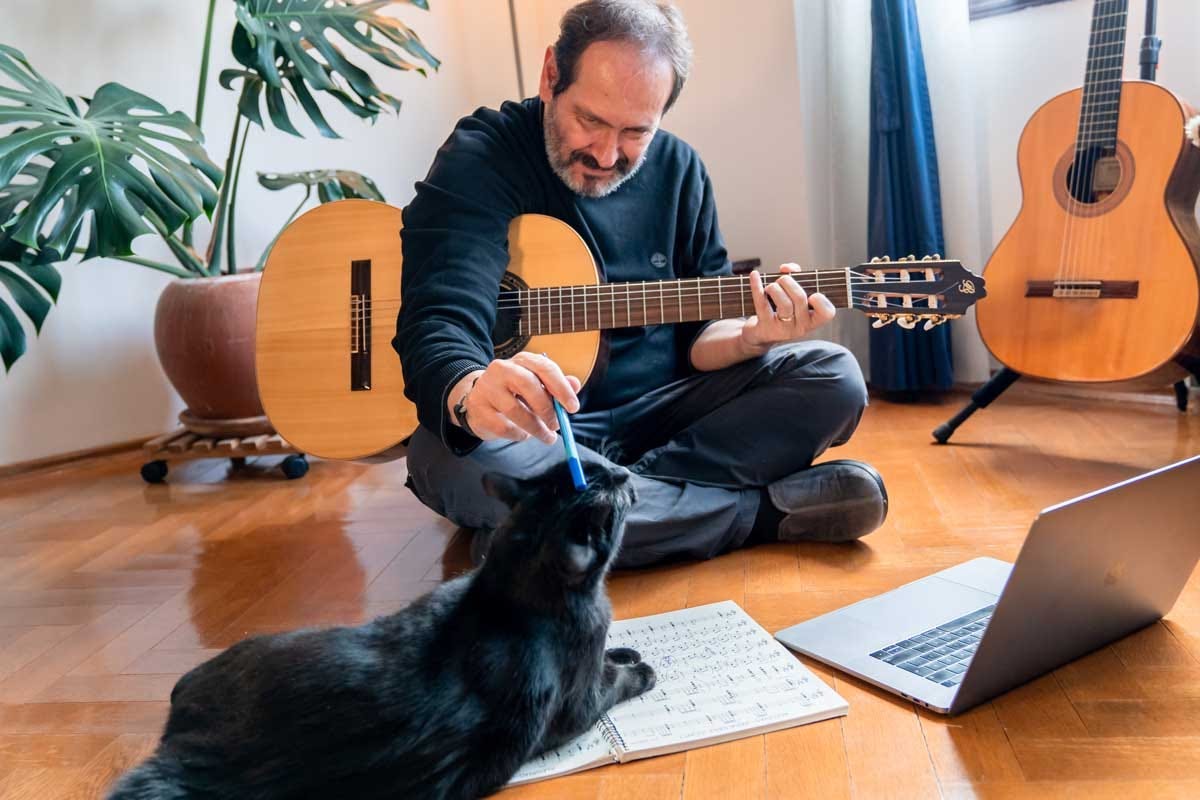 Elder gentleman playing with his cat while practicing guitar.