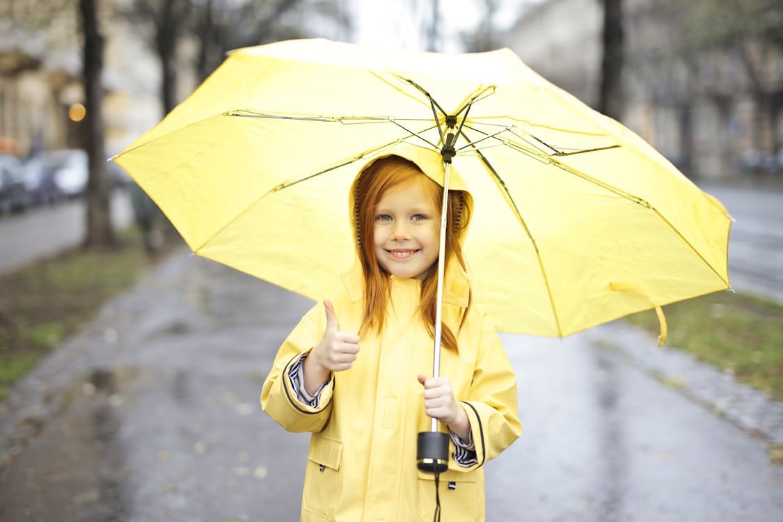 Free Photo of Smiling Girl in Yellow Raincoat Holding a Yellow Umbrella While Giving One Thumbs Up Stock Photo