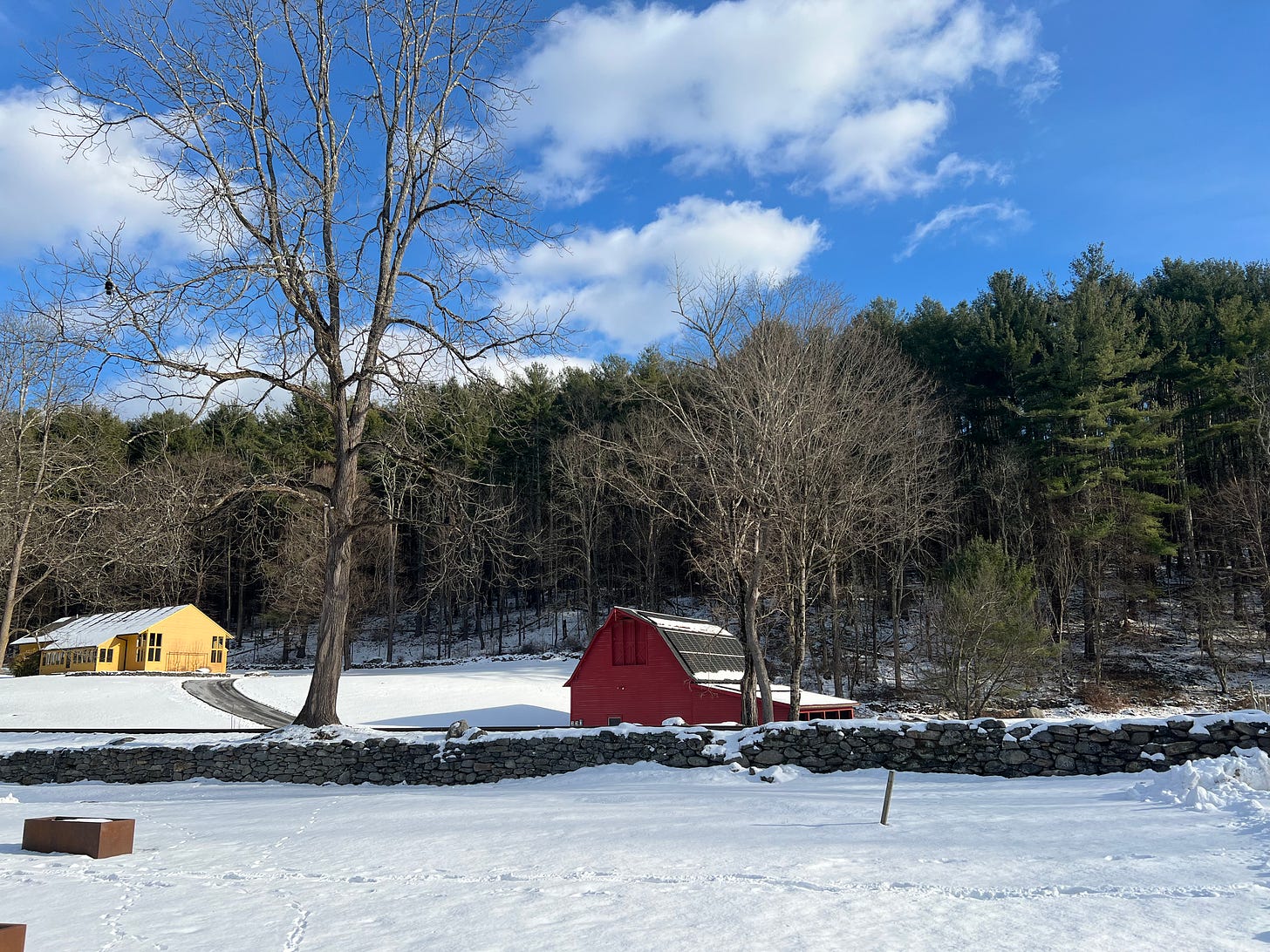 Pic of a red barn and yellow house with trees in the background and snow on the ground