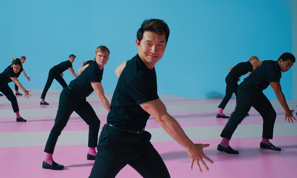 Simu Liu como Ken dançando lindamente todo de preto com vários outros Kens sincronizados ao fundo
