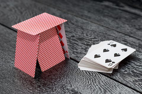 A pack of cards sitting next to a card tower on a black table cloth