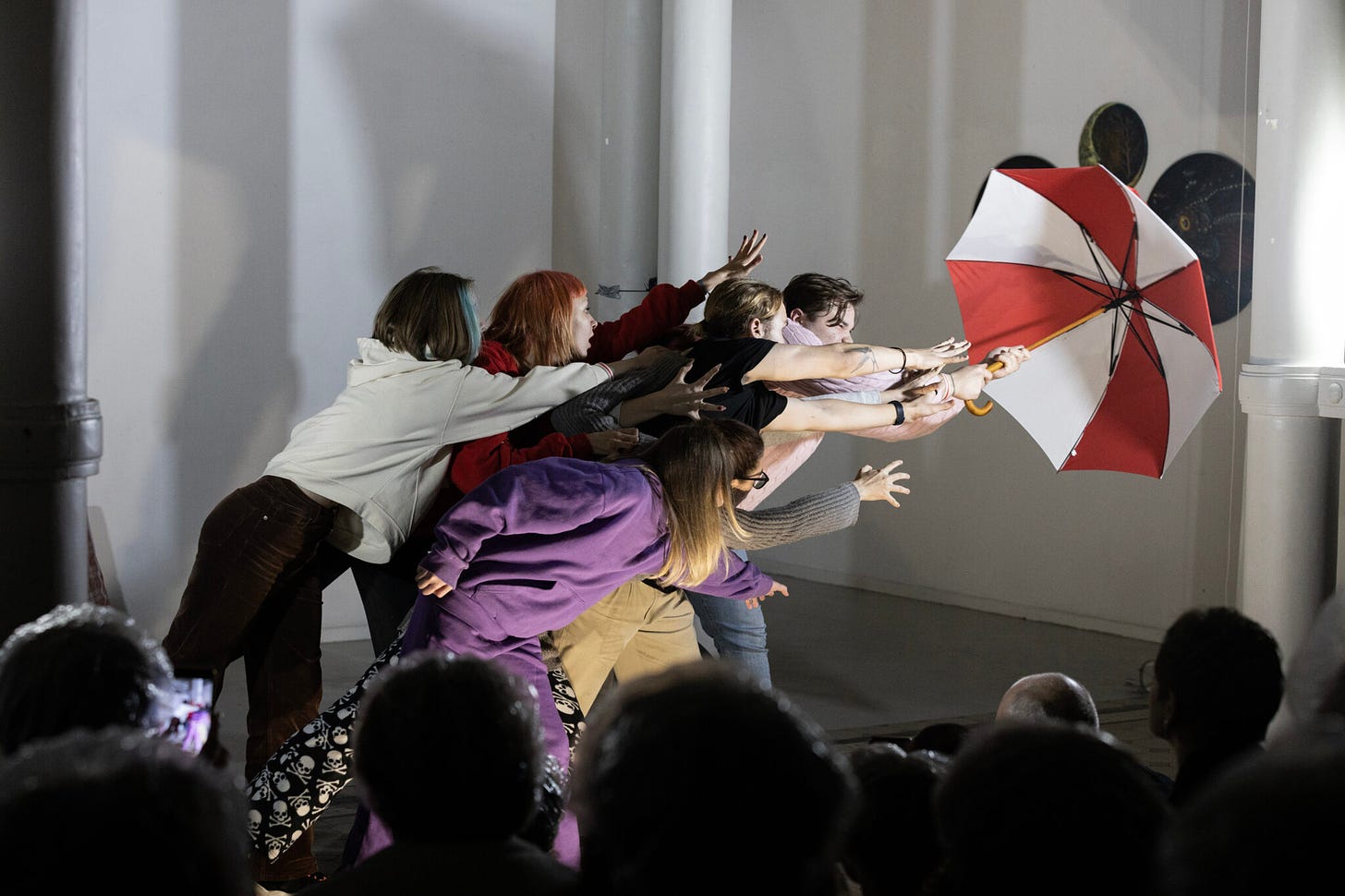 A group of children cling onto a red and white striped umbrella.