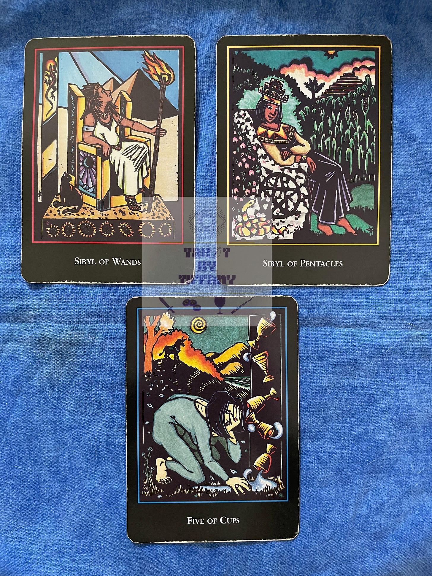 3-card reading with the World Spirit Tarot. The cards are laid out on a cobalt blue cloth background. Top two cards (L-R): Sibyl of Wands and Sibyl of Pentacles. Bottom card: 5 of Cups.