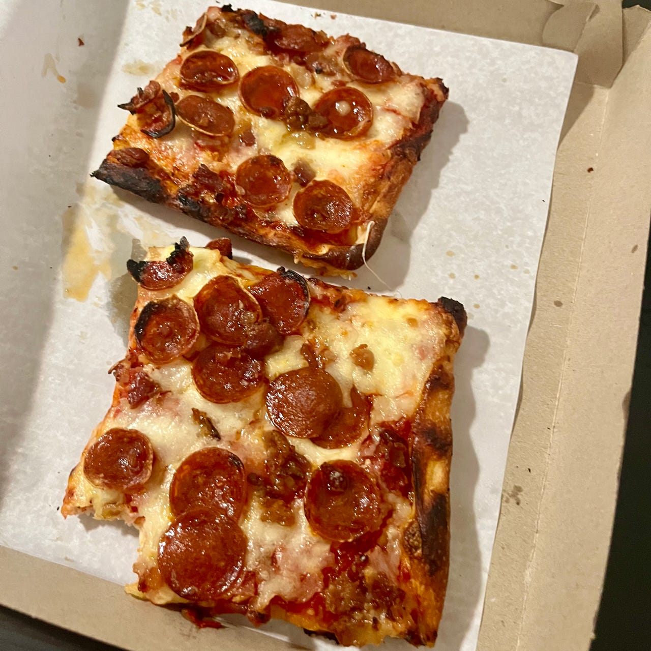 two square slices of pizza topped with greasy pepperoni inside a cardboard box.