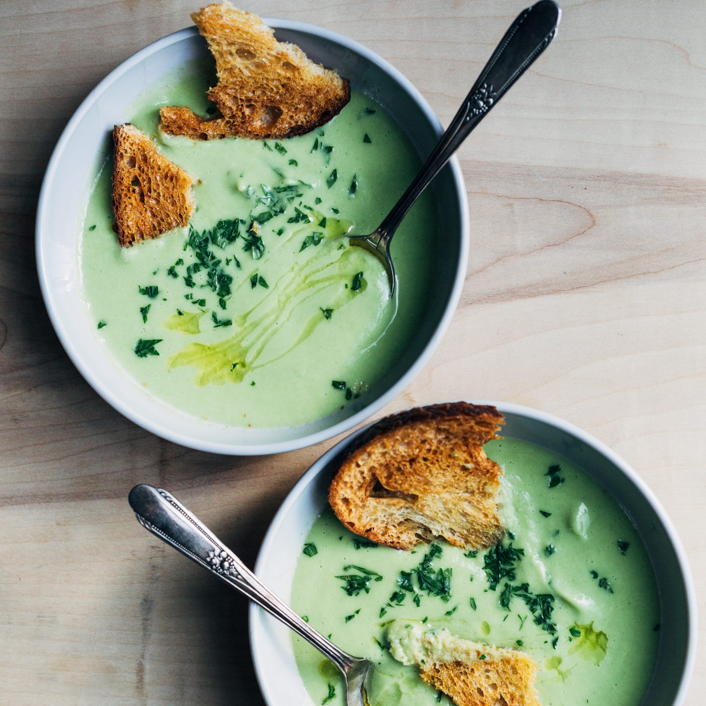 Two bowls of green cauliflower-leek soup with golden croutons and a drizzle of olive oil.