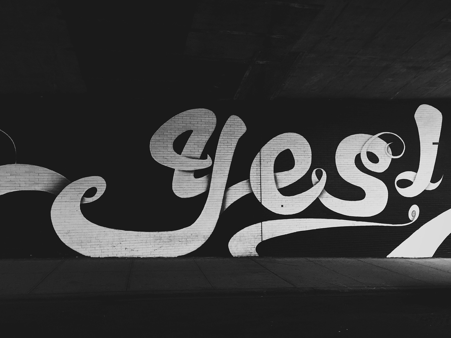 A black and white photo of grafitti on a wall that says 'yes' in fancy coca cola cursive