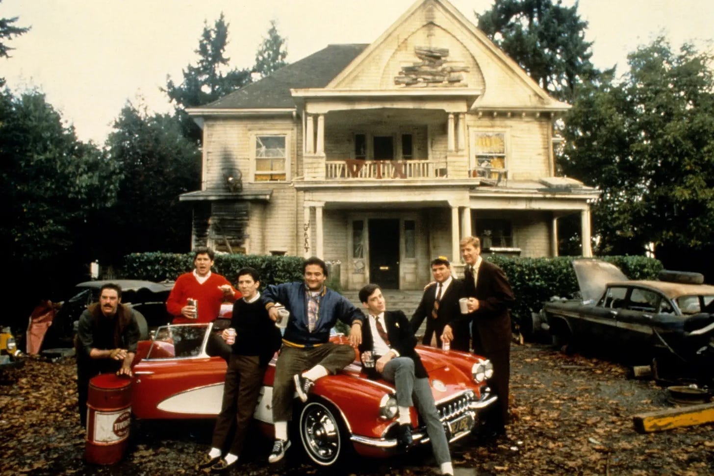 From the famous movie Animal House, set at a fictional college in 1962, the group of young men living lives of extreme debauchery poses around a car in front of a dilapidated frat house.