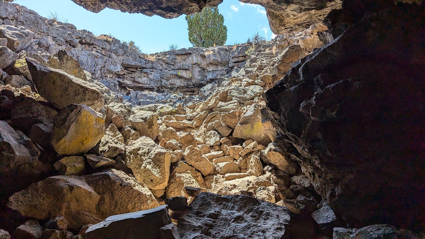 Yellow and grey rocks inside a lava tube cave entrance, the sky barely visible beyond