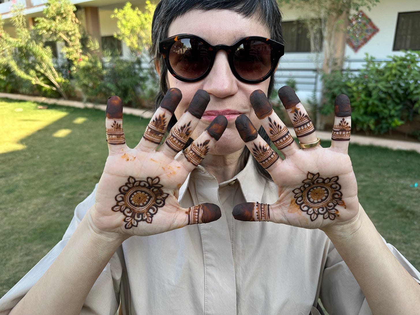 Mulher com óculos escuros mostrando as palmas das mãos decoradas com desenhos de henna.