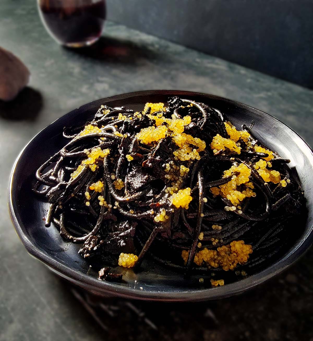 A plate of black pasta with caviar on a dark background.
