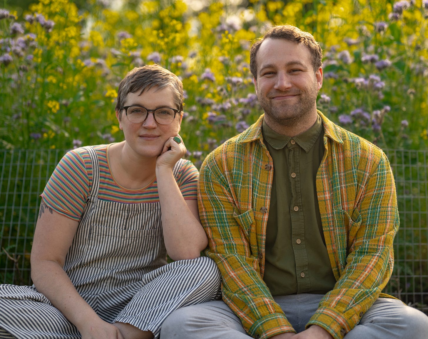 two middle aged white people are sitting in front of a field of wildflowers. 