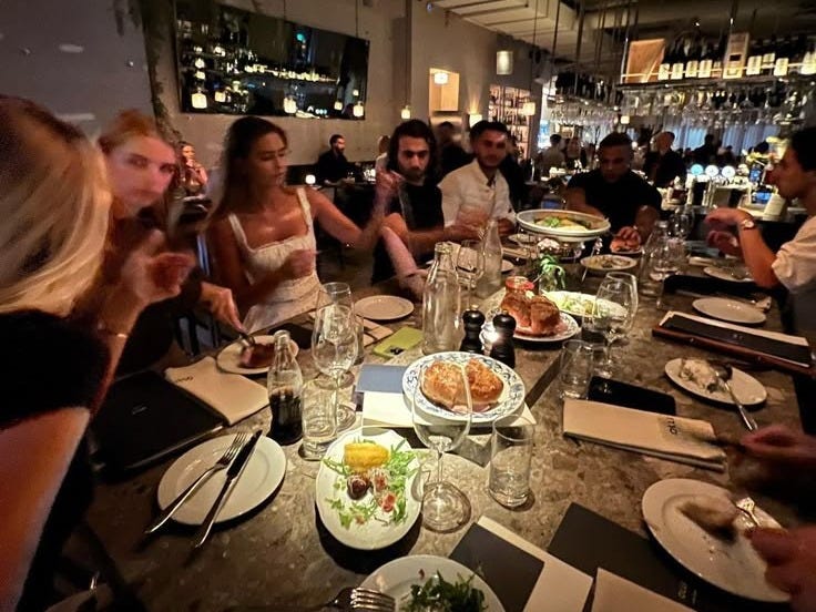 This may contain: a group of people sitting at a table with plates of food in front of them