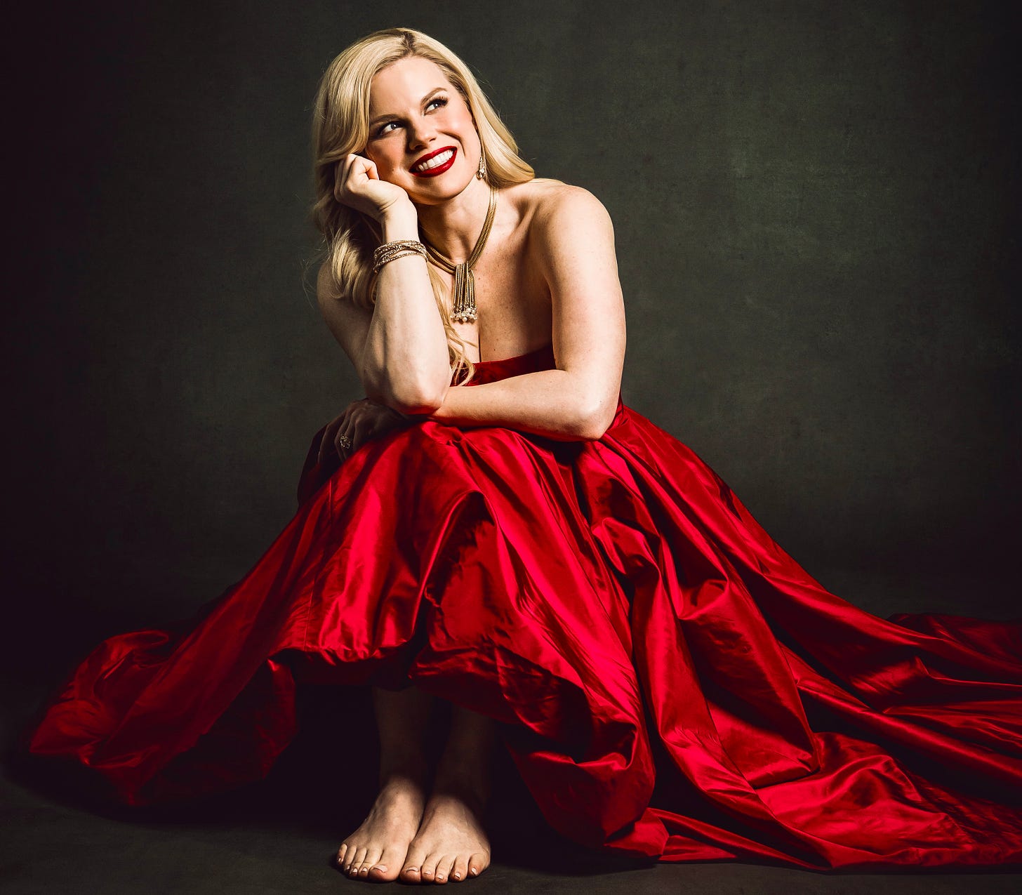 A smiling blonde woman in bare feet and a red satin dress